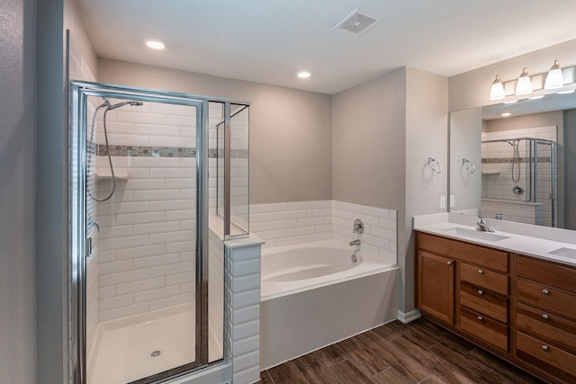 bathroom with visible vents, wood finished floors, a bath, a shower stall, and a sink