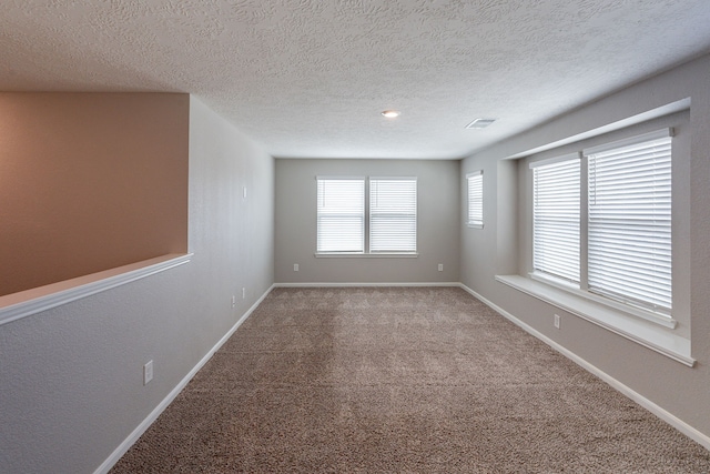 empty room featuring carpet floors, a textured ceiling, baseboards, and visible vents