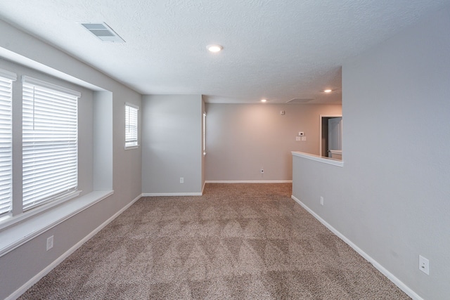 empty room featuring a textured ceiling, visible vents, baseboards, carpet, and recessed lighting