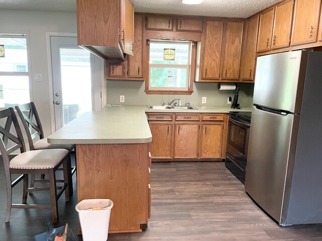kitchen featuring black range with electric stovetop, light countertops, a sink, freestanding refrigerator, and a peninsula