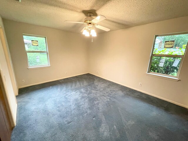 empty room with dark colored carpet, a ceiling fan, a textured ceiling, and baseboards