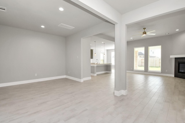 unfurnished living room featuring a glass covered fireplace, a ceiling fan, baseboards, light wood-type flooring, and visible vents