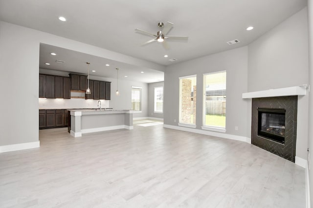unfurnished living room with visible vents, baseboards, ceiling fan, a tile fireplace, and a sink