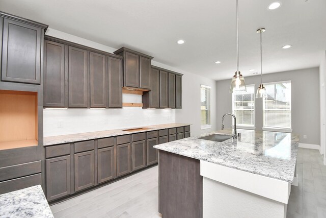 kitchen with light stone countertops, a sink, a kitchen island with sink, recessed lighting, and light wood-type flooring