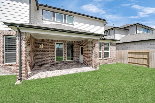 back of house with brick siding, a lawn, fence, and a patio