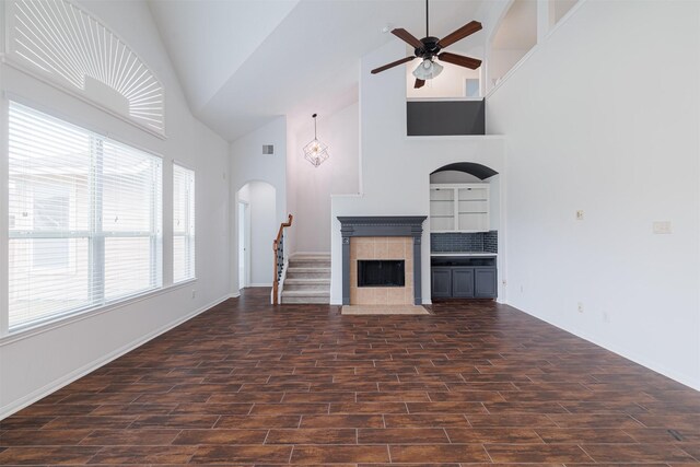 unfurnished living room with dark wood-style flooring, ceiling fan, a fireplace, arched walkways, and high vaulted ceiling