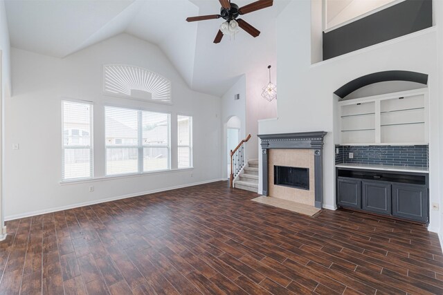 unfurnished living room with ceiling fan, high vaulted ceiling, baseboards, a tile fireplace, and dark wood-style floors