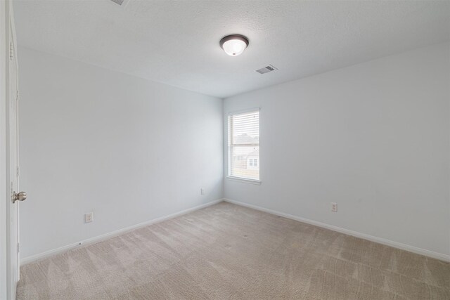 empty room with a textured ceiling, baseboards, visible vents, and light carpet