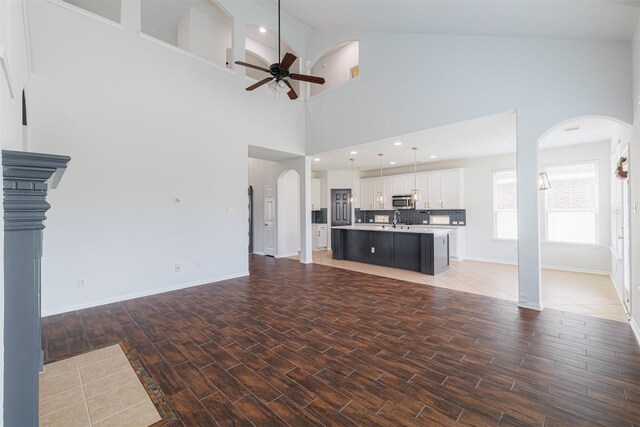 unfurnished living room featuring ceiling fan, a sink, arched walkways, baseboards, and wood finished floors