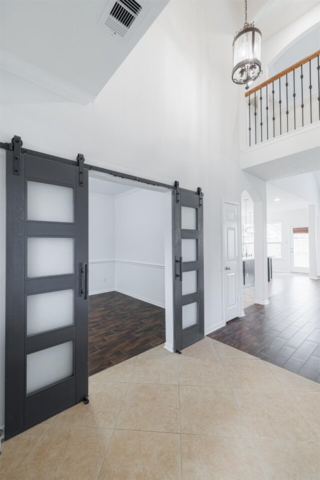 foyer entrance featuring visible vents, a towering ceiling, tile patterned flooring, a barn door, and a chandelier