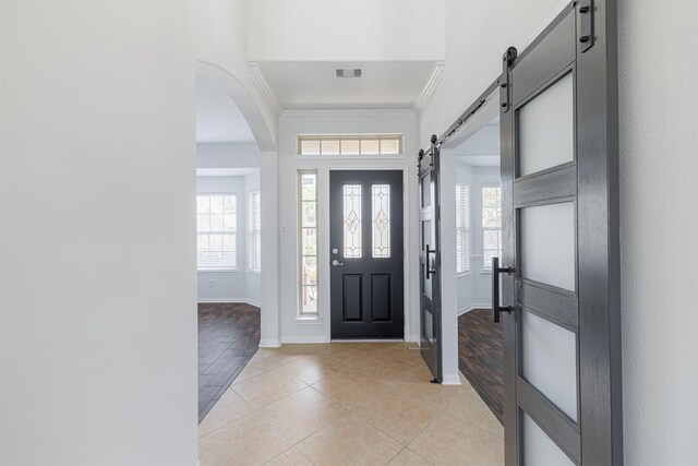 entryway featuring crown molding, a barn door, baseboards, and light tile patterned floors