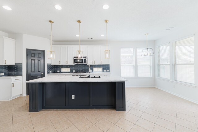 kitchen featuring a sink, white cabinetry, stainless steel microwave, light tile patterned floors, and backsplash
