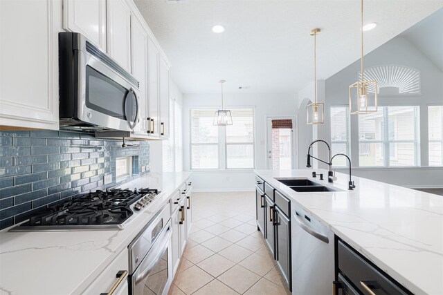 kitchen featuring light tile patterned flooring, baseboards, white cabinets, a sink, and appliances with stainless steel finishes
