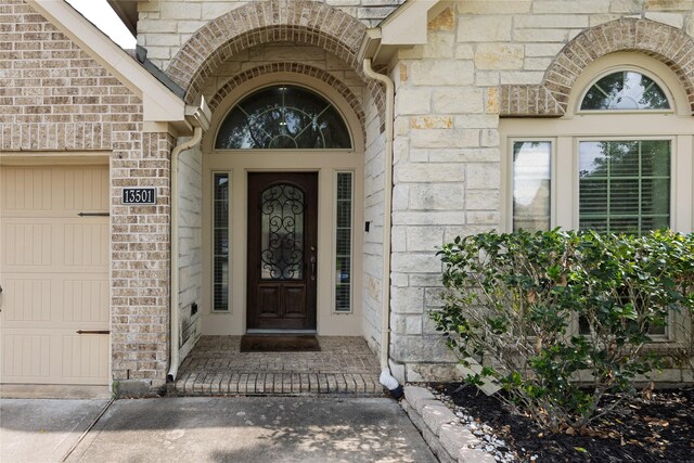 doorway to property featuring brick siding, a garage, and stone siding