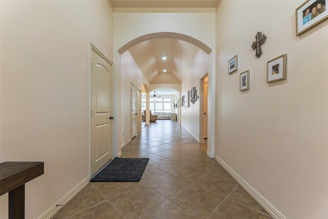 corridor with arched walkways, baseboards, tile patterned flooring, and lofted ceiling