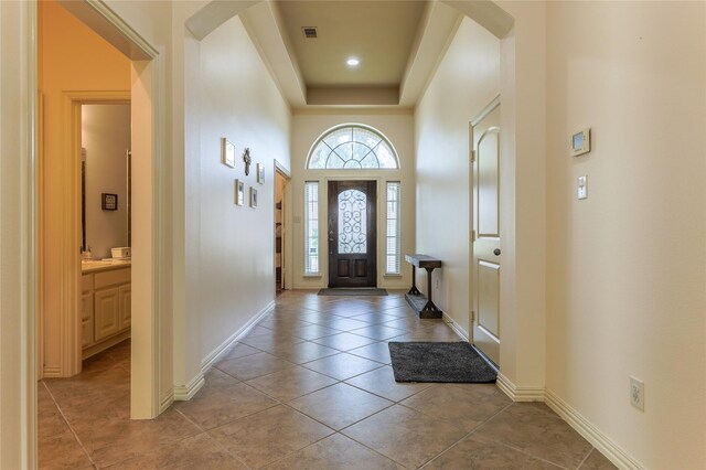 foyer featuring baseboards, a tray ceiling, light tile patterned flooring, and visible vents