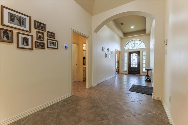entryway with arched walkways, baseboards, visible vents, and a raised ceiling