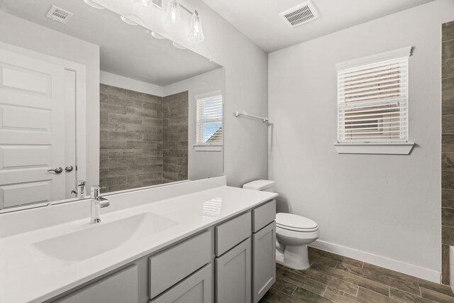 bathroom featuring vanity, toilet, baseboards, wood finished floors, and visible vents