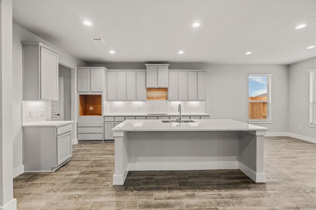 kitchen with a sink, a kitchen island with sink, light wood-type flooring, backsplash, and visible vents