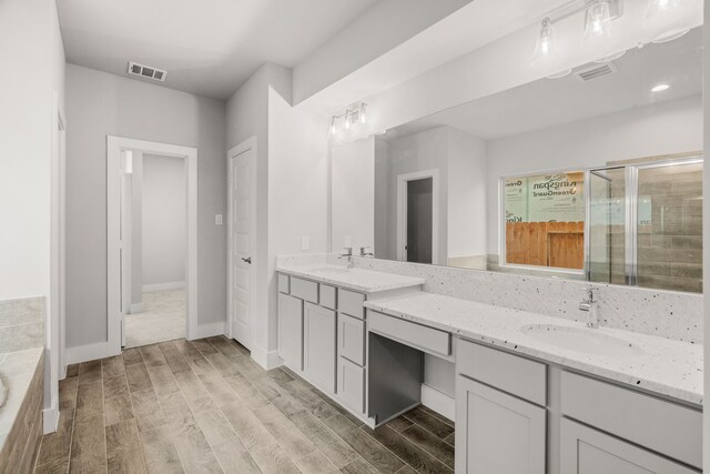 bathroom with a sink, double vanity, wood finished floors, visible vents, and a stall shower