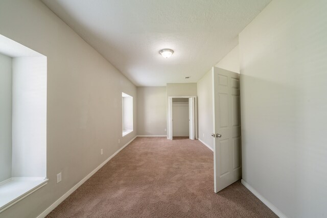 interior space with a textured ceiling, baseboards, and light colored carpet