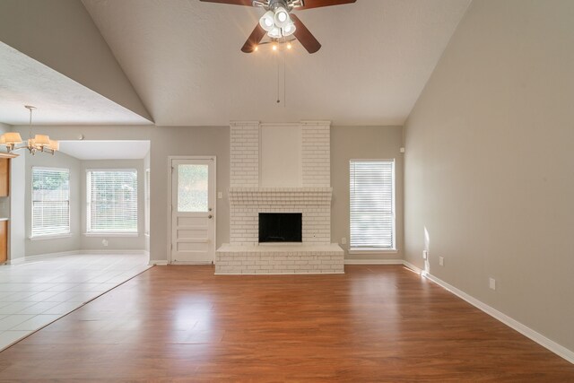 unfurnished living room with wood finished floors, a fireplace, baseboards, ceiling fan with notable chandelier, and vaulted ceiling