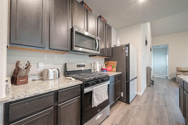 kitchen featuring dark brown cabinetry, light stone countertops, light wood finished floors, stainless steel appliances, and baseboards