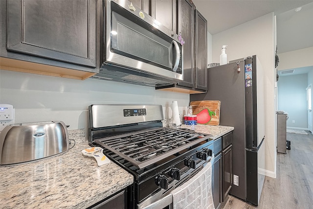 kitchen featuring light stone countertops, stainless steel appliances, light wood-style flooring, and dark brown cabinetry