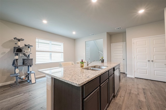kitchen with dark brown cabinets, a sink, light wood finished floors, stainless steel dishwasher, and visible vents