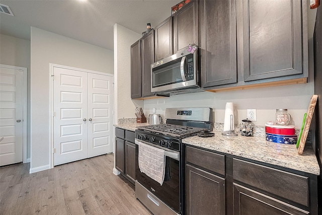 kitchen featuring appliances with stainless steel finishes, dark brown cabinetry, light wood finished floors, and light stone counters