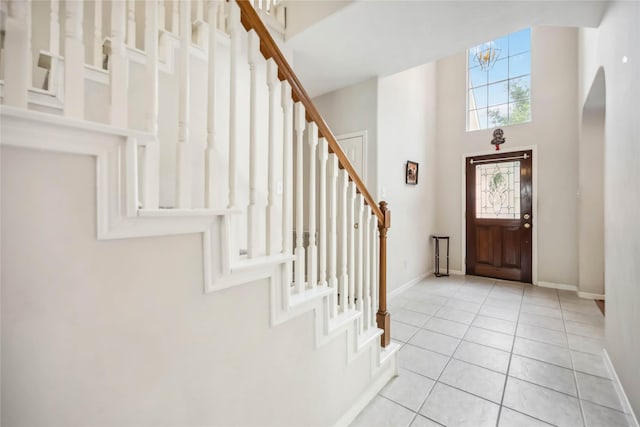foyer with stairs, light tile patterned flooring, baseboards, a high ceiling, and arched walkways