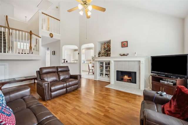 living room with a ceiling fan, arched walkways, wood finished floors, and a tile fireplace