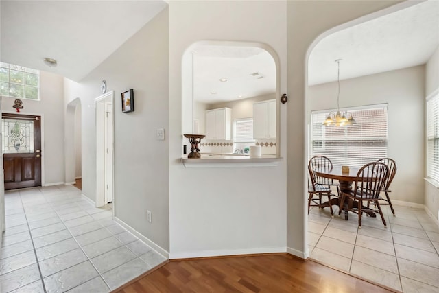 corridor with baseboards, arched walkways, light tile patterned flooring, and a chandelier