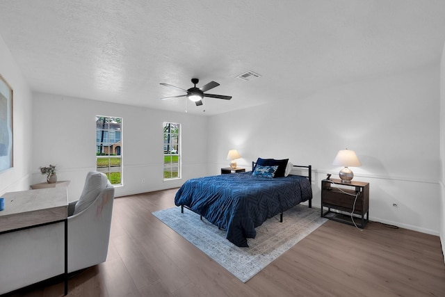 bedroom with visible vents, wood finished floors, baseboards, ceiling fan, and a textured ceiling