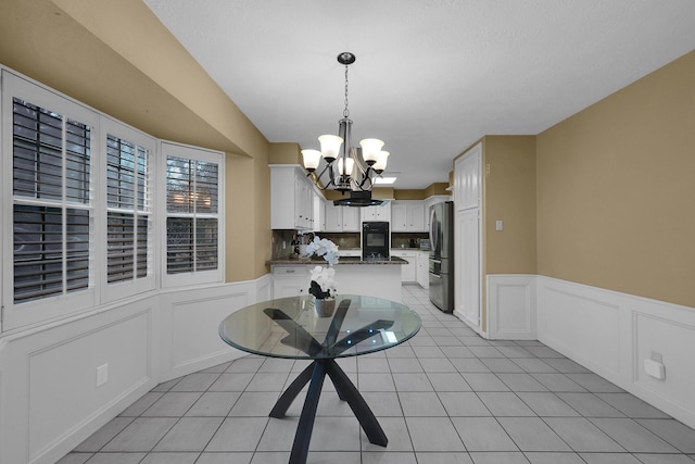 dining space featuring light tile patterned floors, a notable chandelier, a wainscoted wall, and a decorative wall