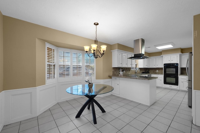 kitchen with dobule oven black, backsplash, island range hood, a sink, and an inviting chandelier