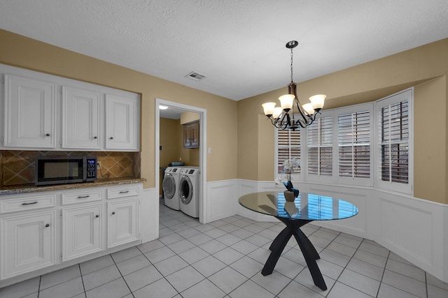 unfurnished dining area with an inviting chandelier, wainscoting, a decorative wall, separate washer and dryer, and visible vents