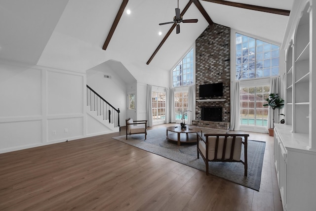 living area featuring beam ceiling, wood finished floors, ceiling fan, high vaulted ceiling, and stairway