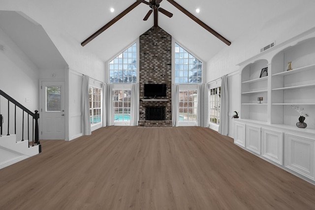 unfurnished living room featuring visible vents, stairs, a brick fireplace, wood finished floors, and a ceiling fan