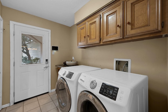 clothes washing area with baseboards, washing machine and dryer, cabinet space, and light tile patterned flooring