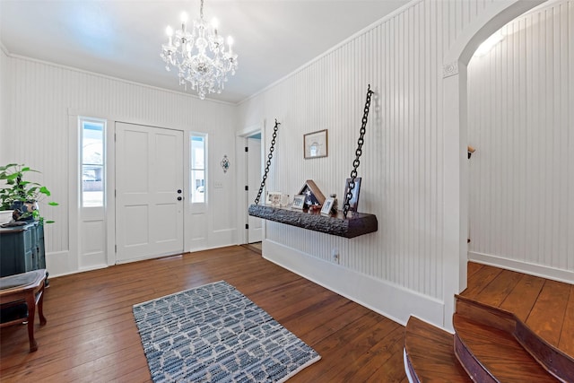 foyer with ornamental molding, arched walkways, a notable chandelier, and hardwood / wood-style flooring