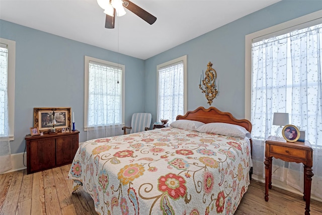 bedroom featuring a ceiling fan, multiple windows, and light wood-style floors