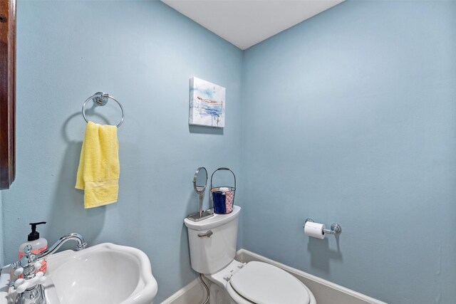 half bathroom with toilet, baseboards, and a sink