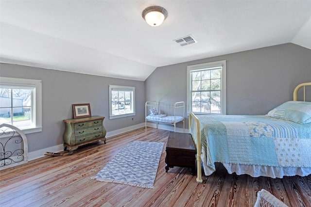 bedroom featuring visible vents, baseboards, wood finished floors, and vaulted ceiling
