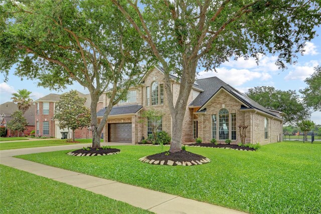 traditional-style home with a garage, brick siding, fence, a front lawn, and concrete driveway