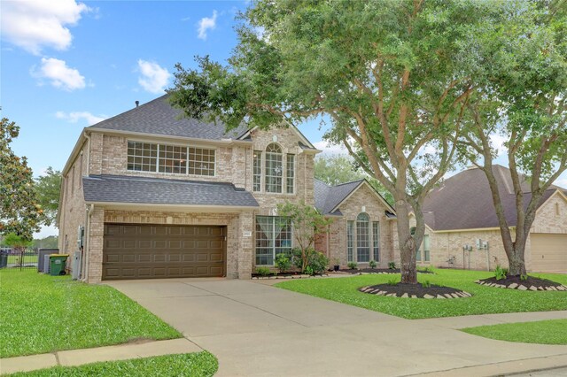 traditional home with a front yard, roof with shingles, brick siding, an attached garage, and driveway