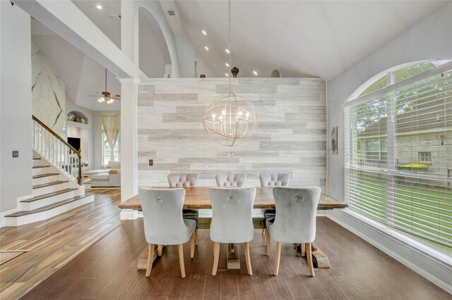 dining room with plenty of natural light, an accent wall, ceiling fan with notable chandelier, and wood finished floors