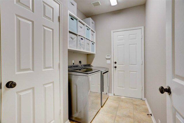 laundry area with laundry area, visible vents, washing machine and dryer, light tile patterned floors, and baseboards