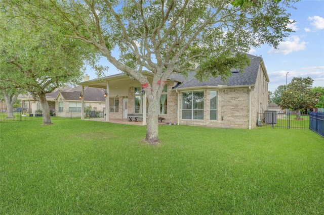back of property with a lawn, a fenced backyard, roof with shingles, and brick siding