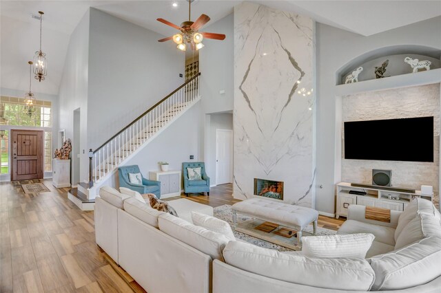 living area featuring ceiling fan, high vaulted ceiling, light wood-style flooring, stairs, and baseboards